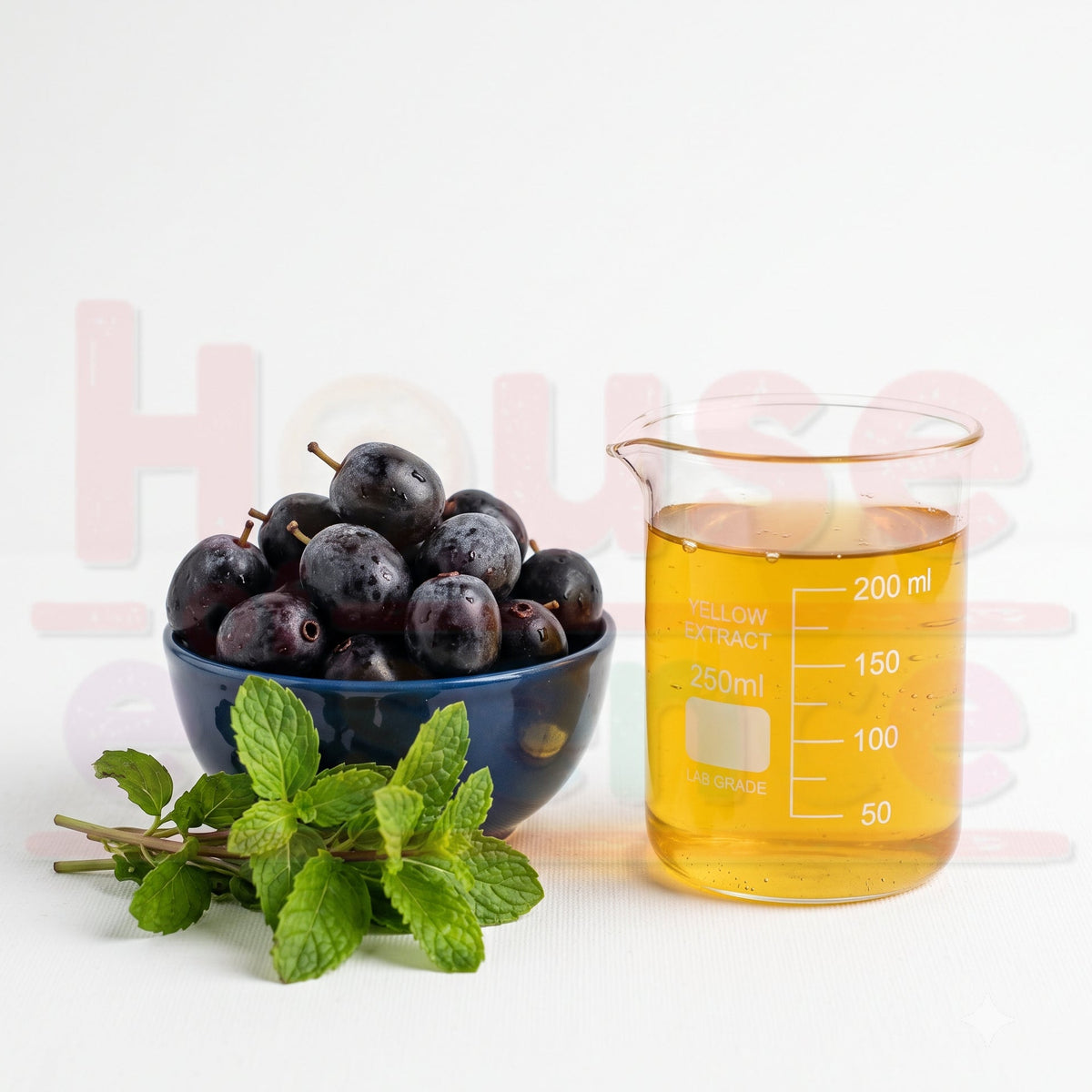 A blue bowl filled with dark purple berries or grapes sits beside a clear glass beaker containing amber-yellow liquid, with fresh green mint leaves in the foreground on a white background.